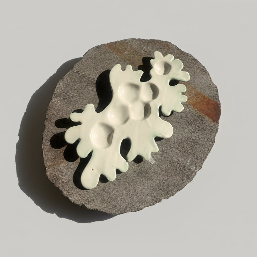 White ceramic earrings on a textured stone surface with shadows cast by leaves.