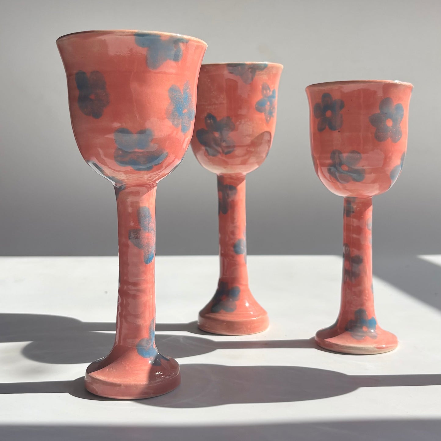 Three ceramic goblets with floral patterns on a white surface and gray background