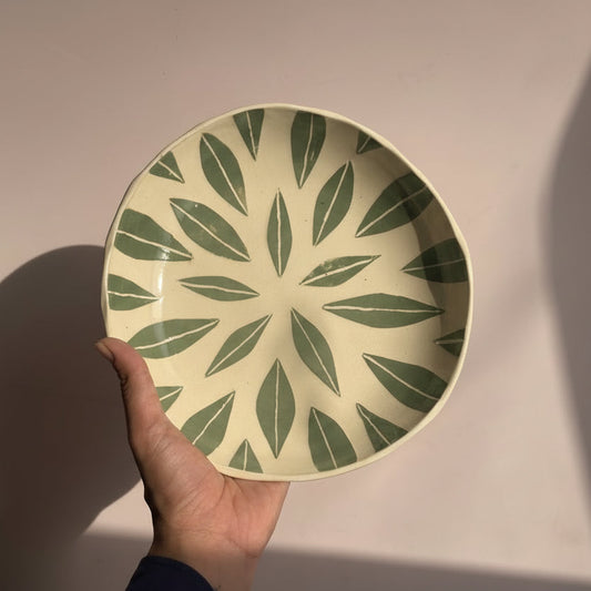 Hand holding a decorative plate with green leaf pattern against a plain background