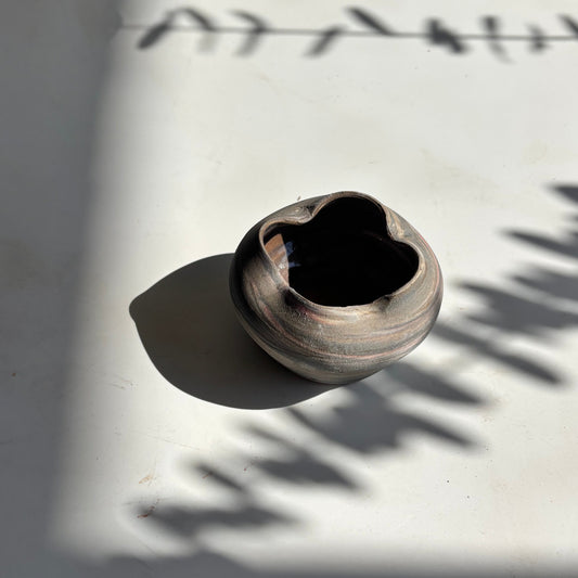 Small ceramic pot on a white surface with shadows cast by leaves.