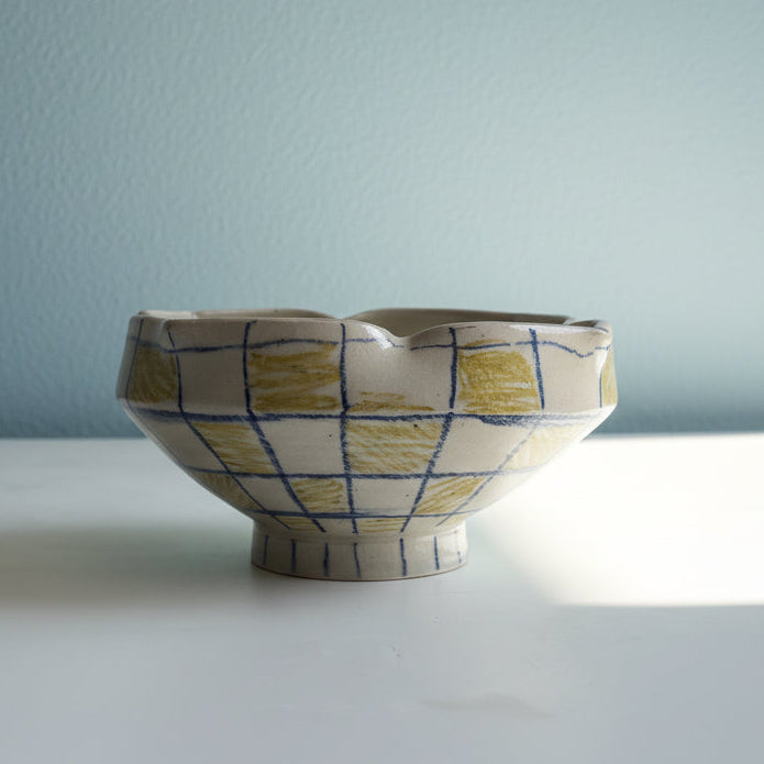 Ceramic bowl with grid pattern on a white surface and light blue wall background