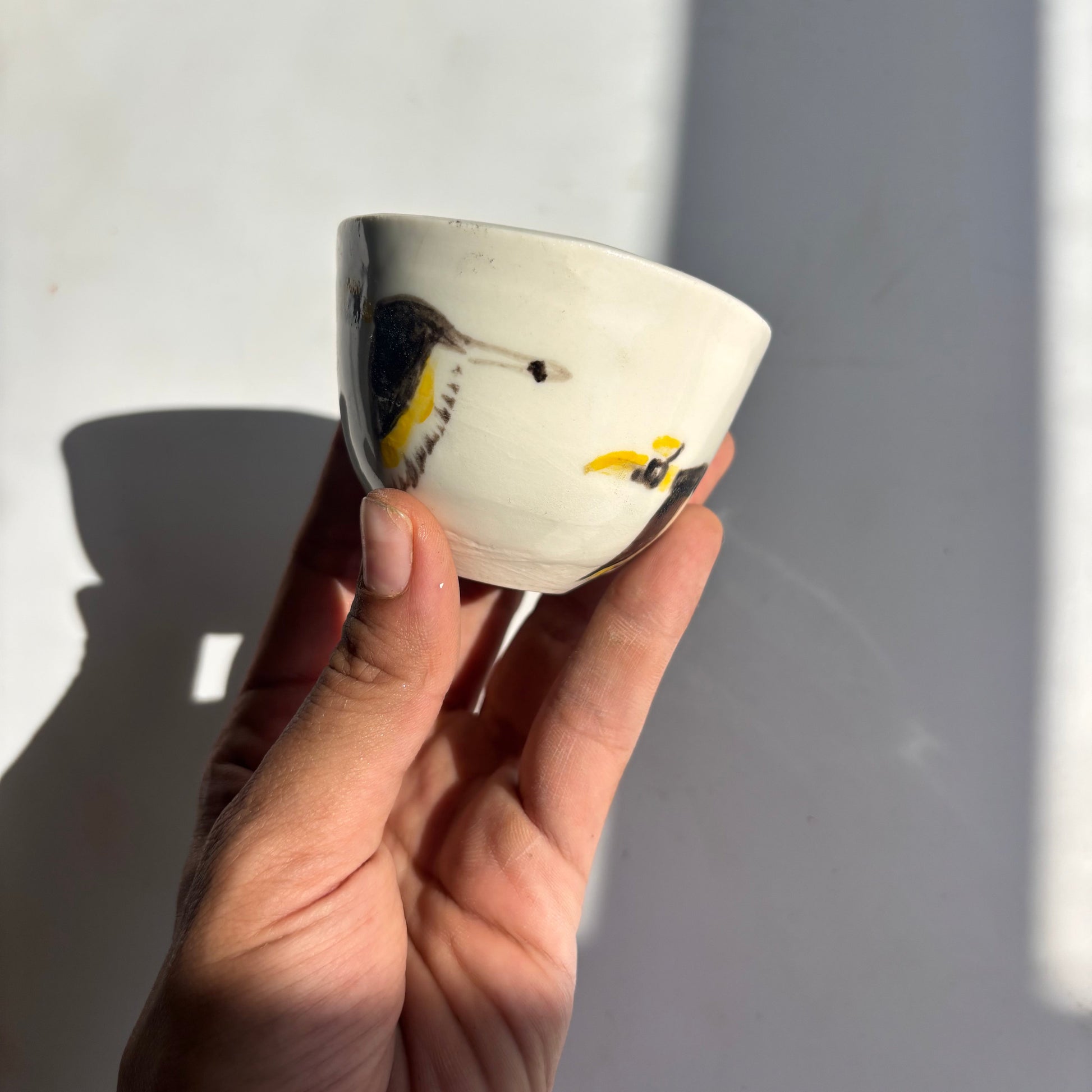 Hand holding a small ceramic cup with butterfly design against a plain background