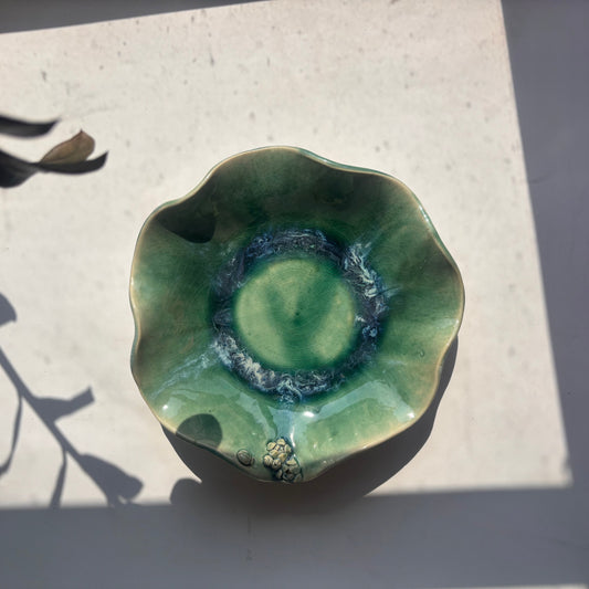 Green ceramic bowl on a light surface with shadows
