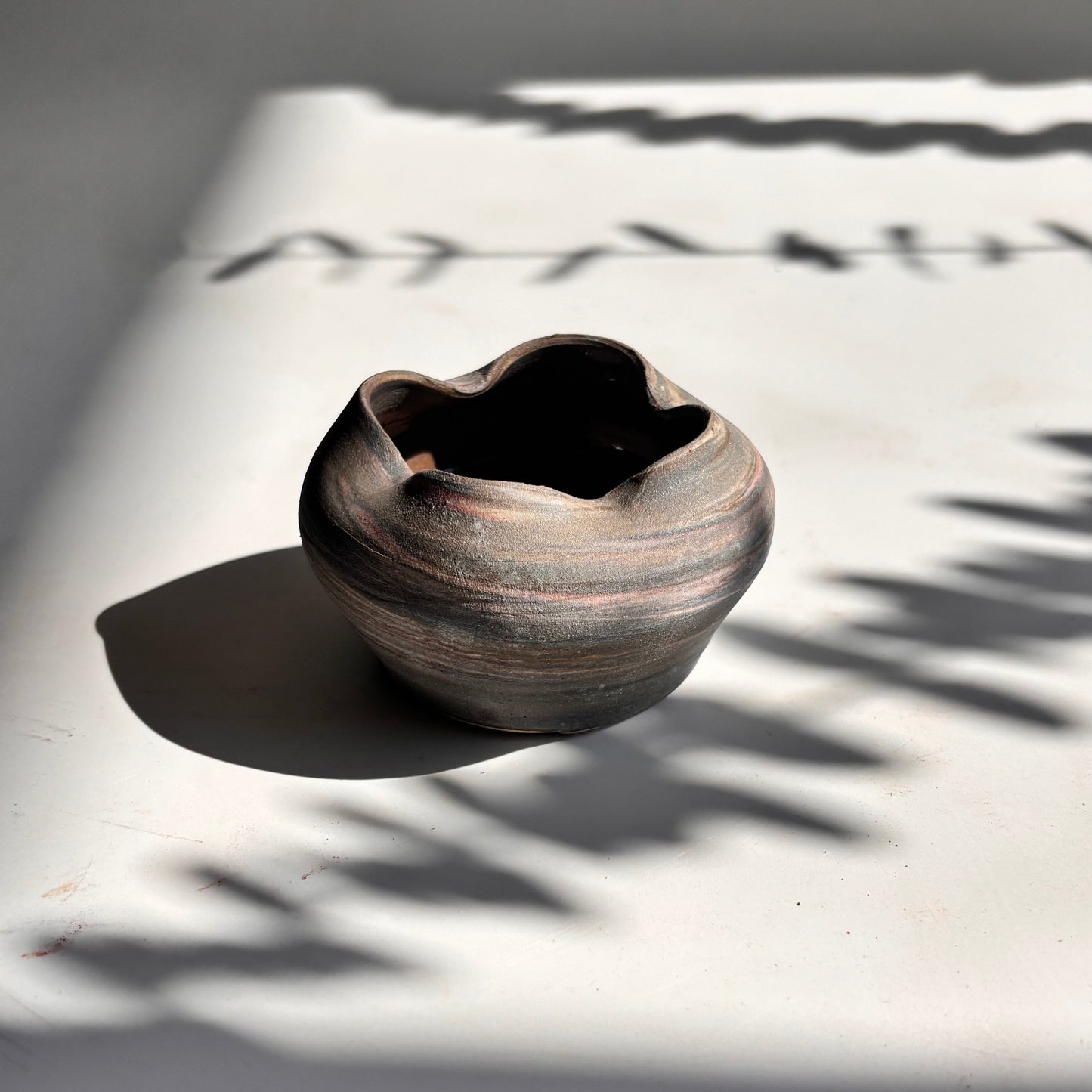 Ceramic bowl on a light surface with shadows from leaves