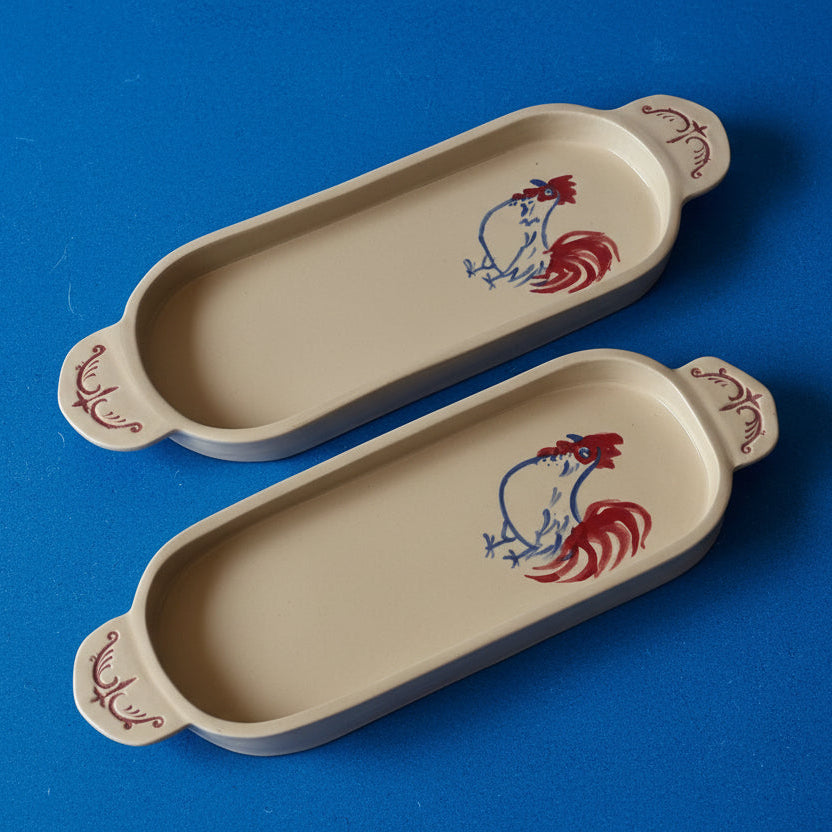 Two ceramic trays with rooster designs on a blue background