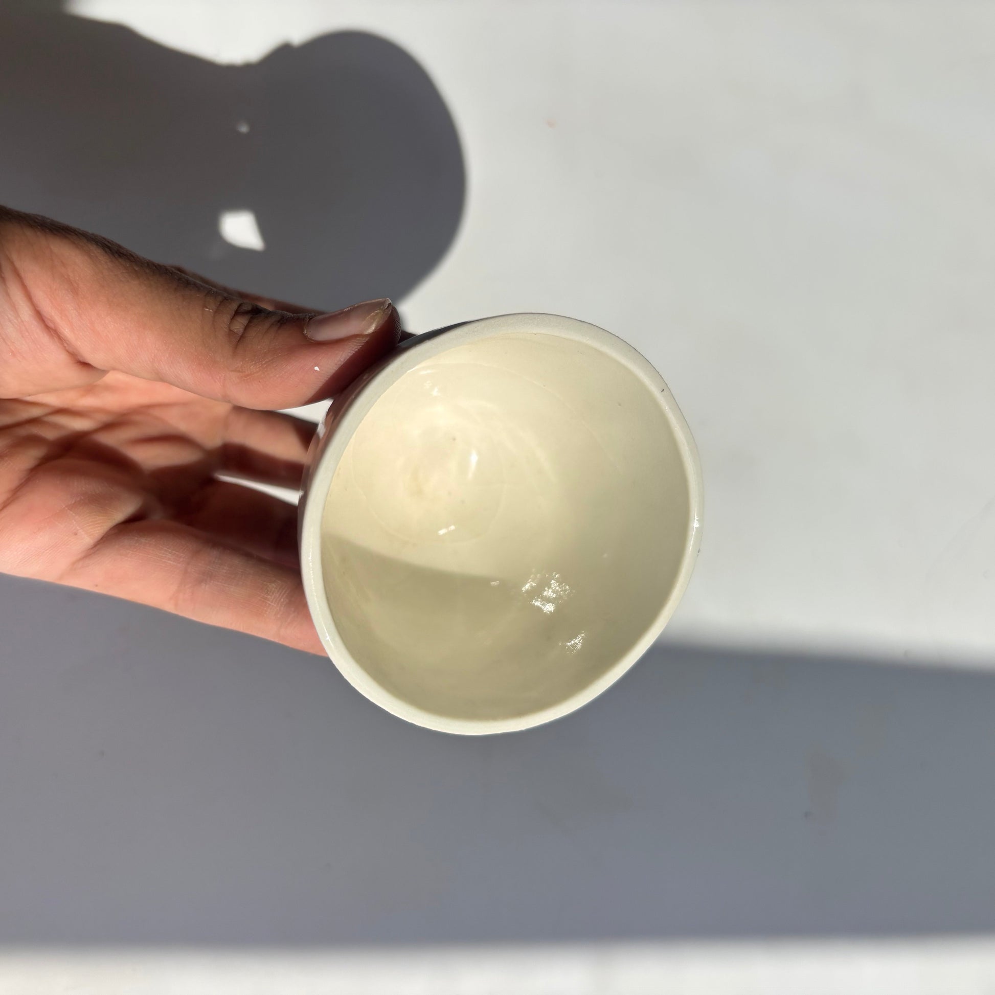 Hand holding a beige ceramic cup against a light gray background