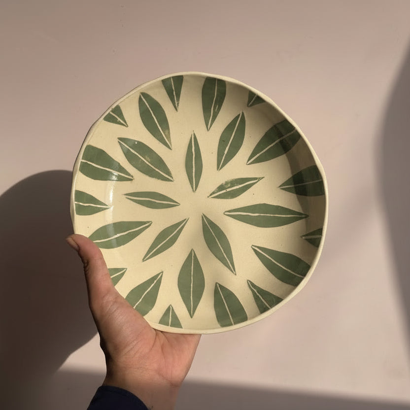 Hand holding a decorative plate with green leaf pattern against a plain background