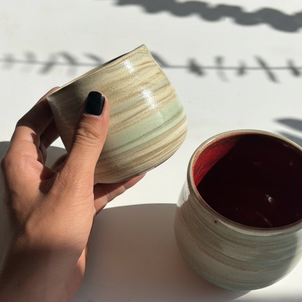 Hand holding a ceramic cup against a white wall with a plant shadow.