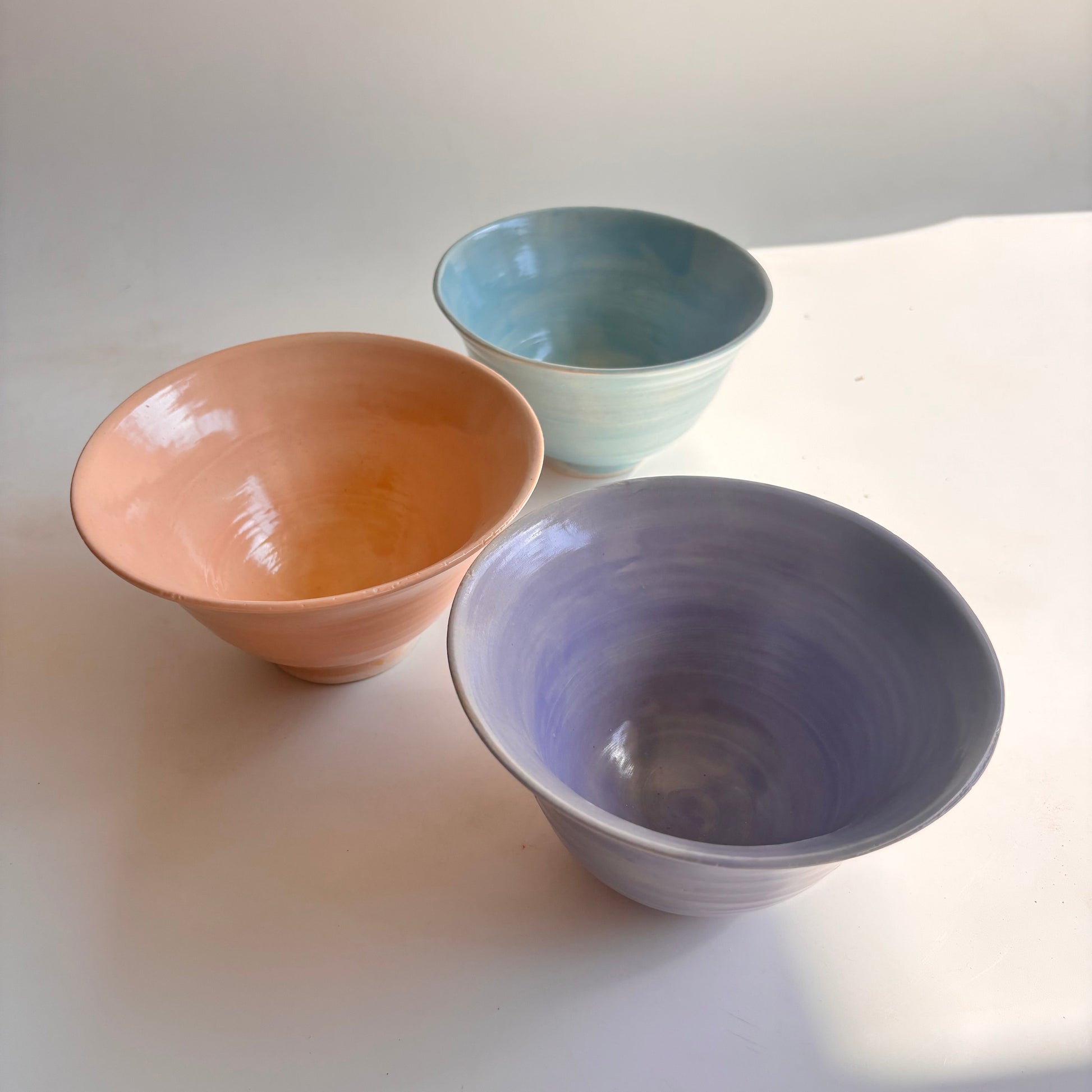 Three ceramic bowls in different colors hanging on a white wall.