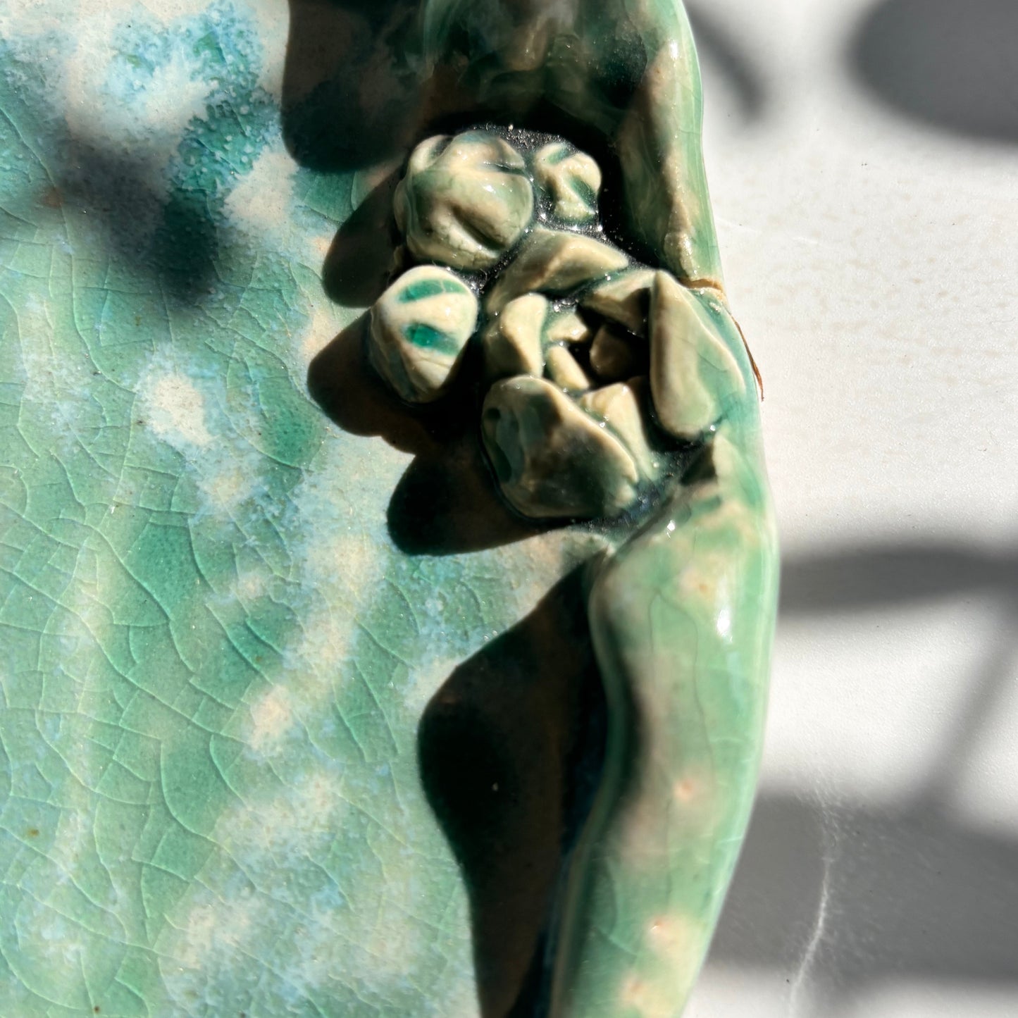 Close-up of a textured green sculpture with a hand holding a flower.