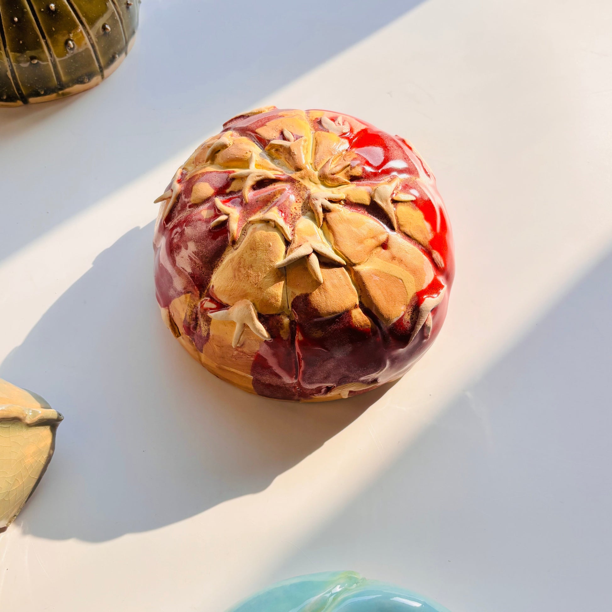 Decorative item resembling a fruit with gold and red patterns on a light surface