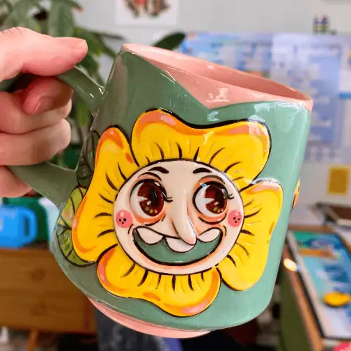 Hand holding a mug with a cartoon sun design in a casual setting